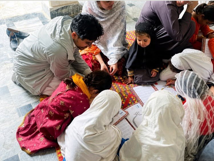 A teacher engaging with students at a desk, books open, focused on their studies.
