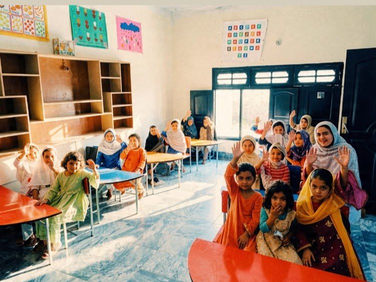 Women and children standing outdoors in a green field as part of a community outreach event.